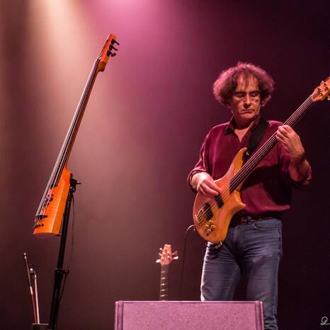 Yann Honore steht auf einer Bühne und ist in pinkem Licht angeleuchtet. Er spielt eine elektrische Gitarre. Und schaut sehr konzentriert und vertieft.