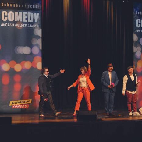 Vier Personen stehen auf einer Bühne. Auf einem Banner steht "Schwabennacht. Comedy aus dem wilden Ländle. Schwäbische  Comedy".
